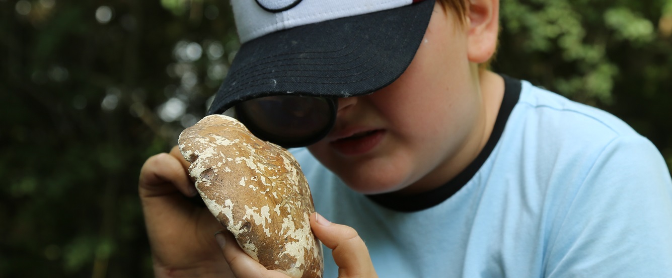 summer camper at Tommy Thompson Park uses a magnifying glass to study local flora