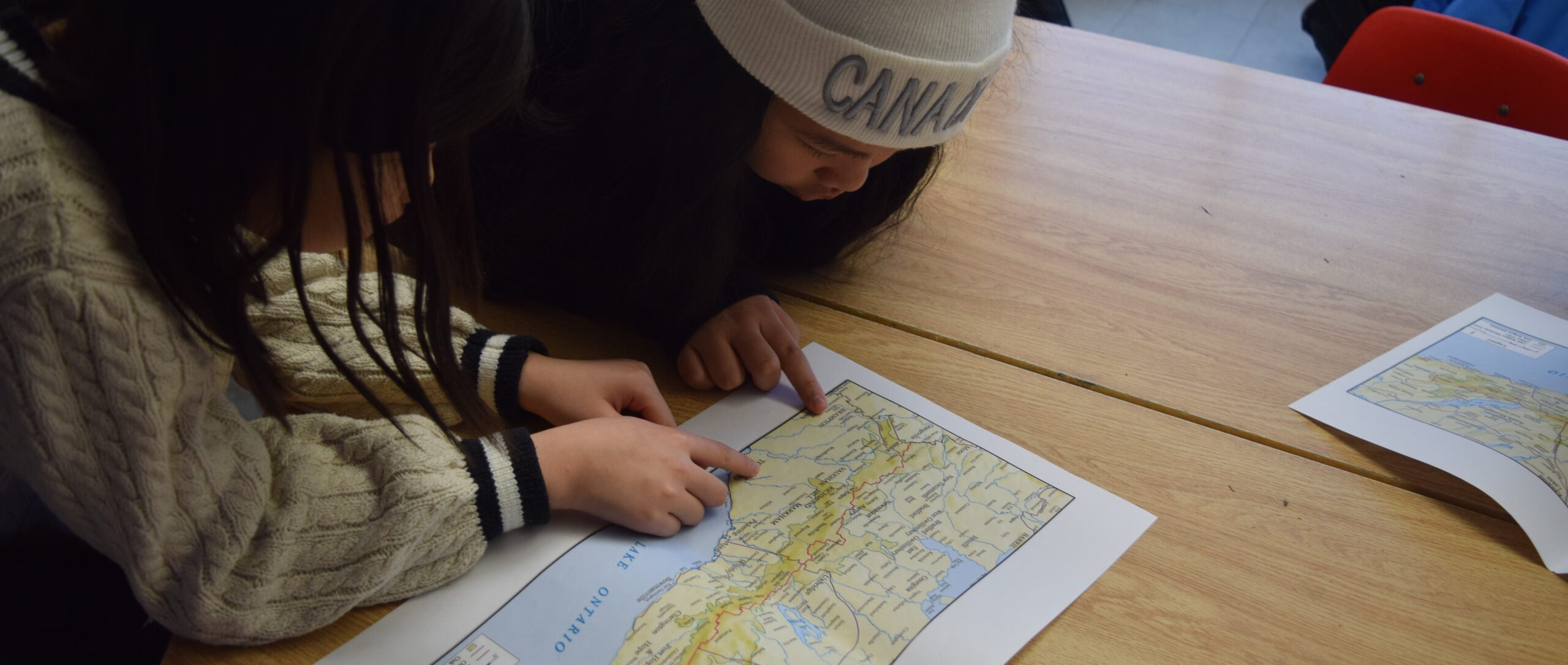 Two students sitting at a table lean intently over a paper map pointing at the page.