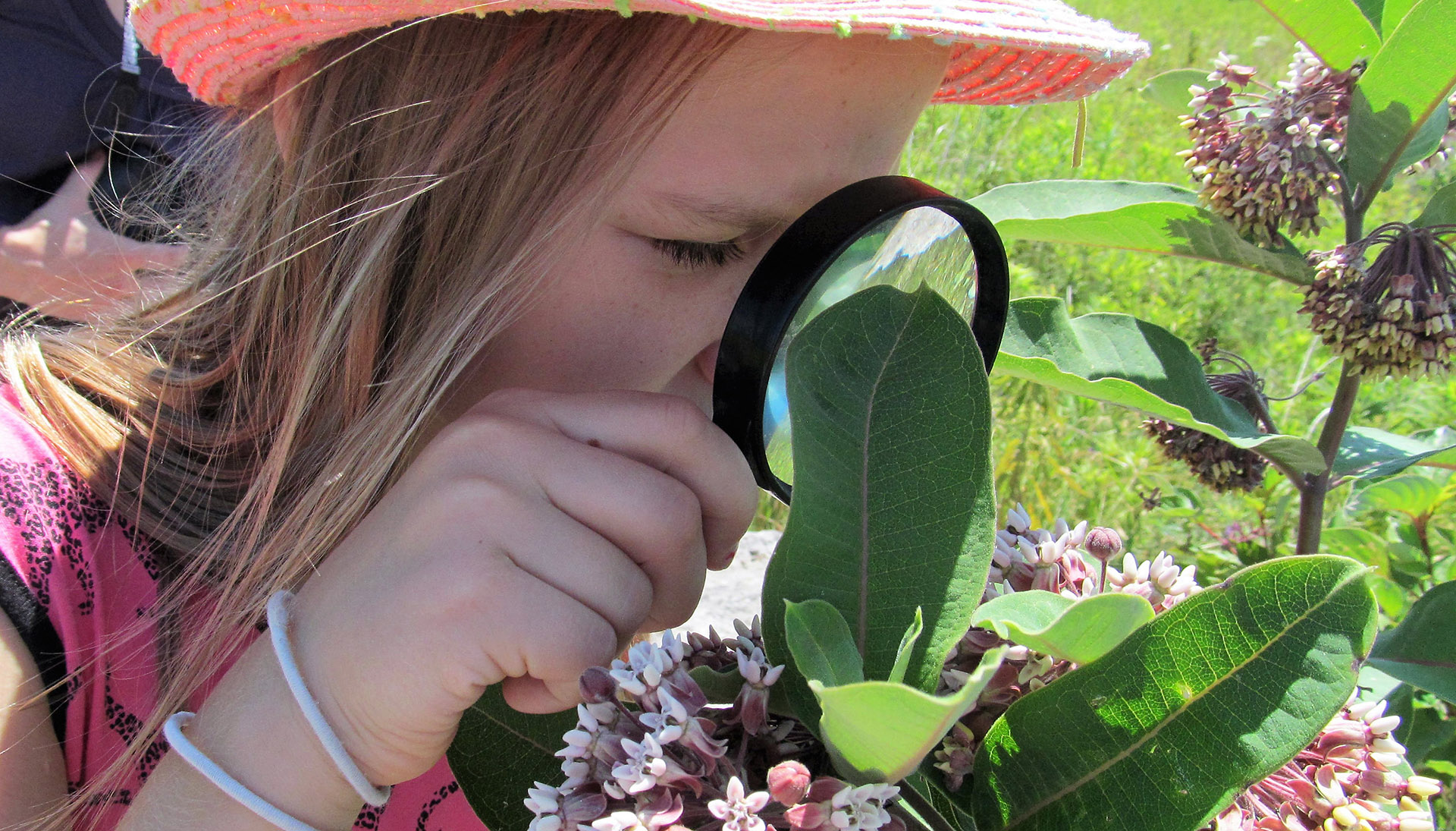 girl inspects plant with magnifying glass