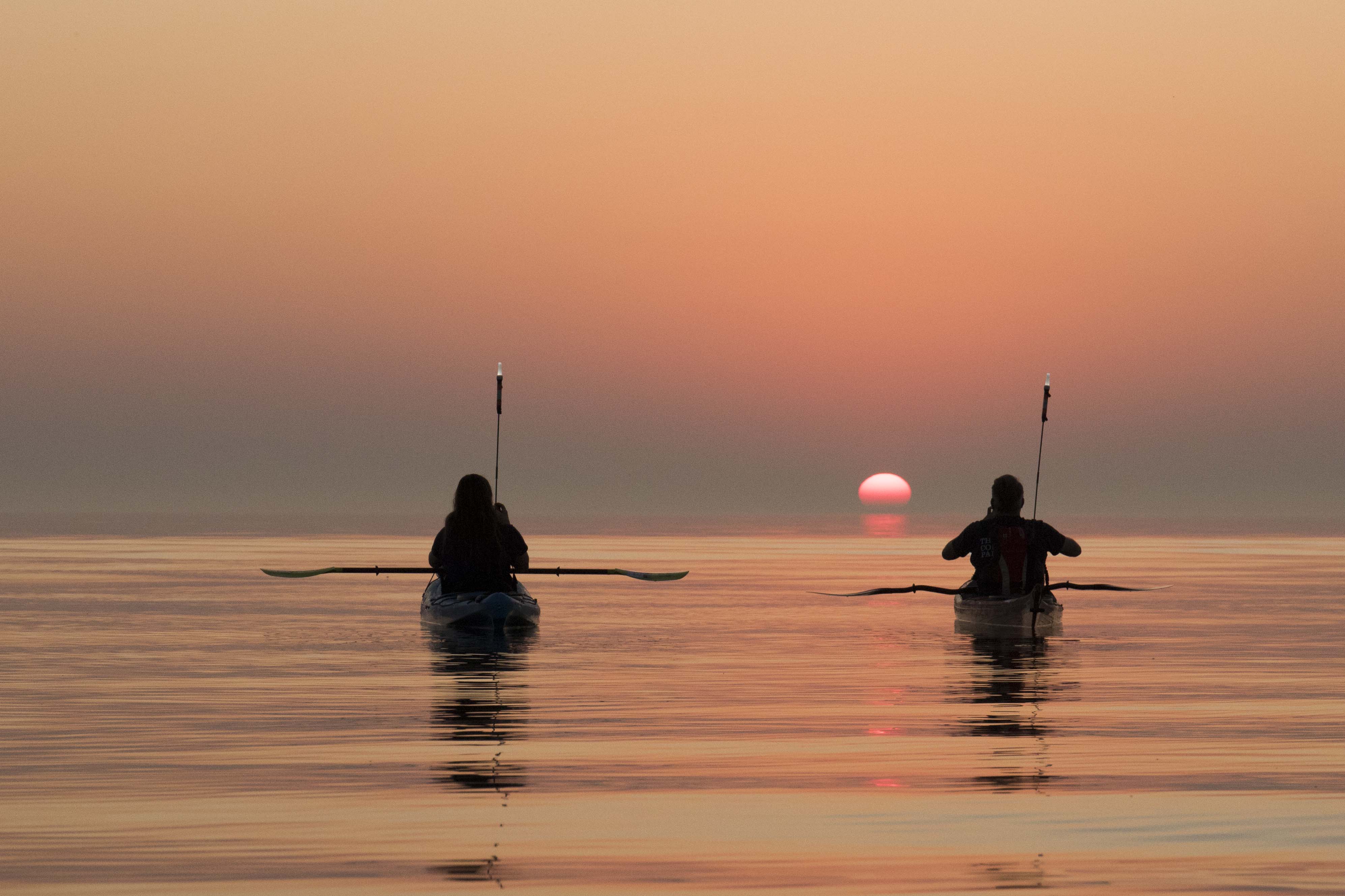 Sitting in kayaks watching the sun rise over the water